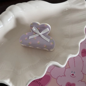 Détail d'une pince à cheveux violette avec motif de pêche et nœud en soie blanche sur plateau