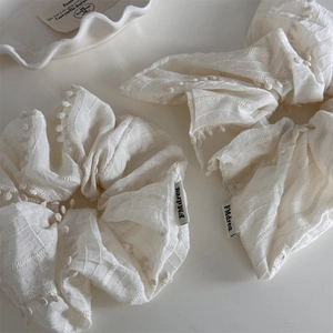 Creamy white fabric scrunchies with 3D dots and brand label on a minimal white tray