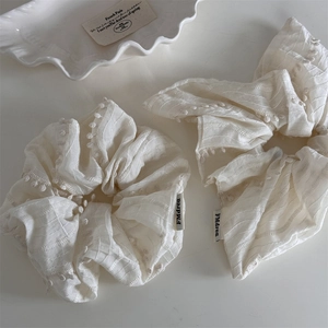 Detailed shot of cream white fabric scrunchie with 3D dots and brand label