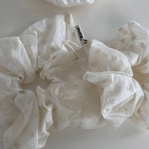 Detailed view of milky white scrunchie with delicate floral daisy embroidery and fabric tag
