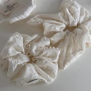 Detailed shot of cream fabric hair scrunchies with soft pom-pom edges and striped texture