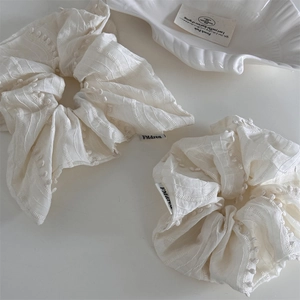 Two white textured fabric scrunchies with raised dots and brand label in minimalist style