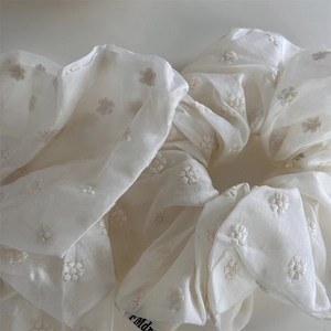 Detail of white organza scrunchie with floral embroidery and elegant fabric texture