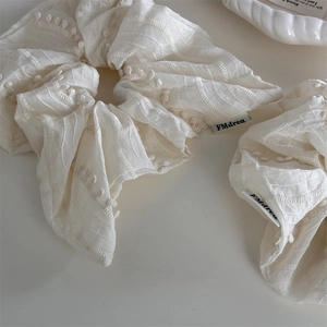 Detail of cream fabric scrunchie featuring 3D dots and embroidered wavy edges