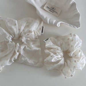 Close-up of cream scrunchie with floral embroidery and French style brand label