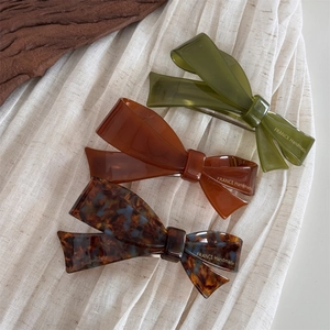 Three elegant acetate bow hair clips in green, amber, and tortoiseshell on white fabric