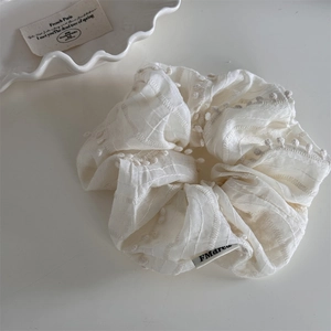 Close-up of cream fabric scrunchie with 3D dots embroidery and ruffled stitching texture