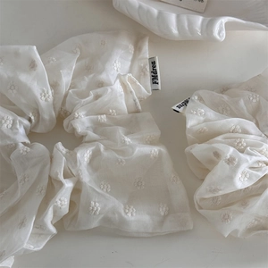 Detail showing white scrunchies with floral daisy embroidery and a small brand label