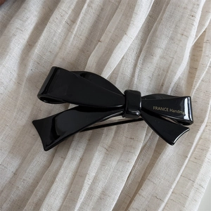Detail of glossy black acetate bow hair clip with gold France Handmade lettering
