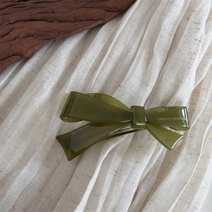 Close-up of olive green acetate bow spring hair clip on elegant wooden texture background