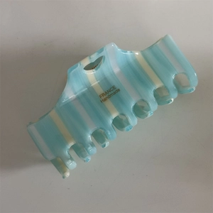 Macro detail of blue striped acetate hair claw clip with golden handmade logo print