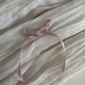 Détail du serre-tête rose avec nœud en soie sur fond en lin ivoire montrant la texture