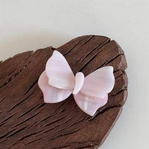 Dettaglio del fermaglio per capelli a farfalla rosa con trama marmorizzata su legno