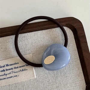 Detailed close-up of blue marble resin hair tie with a gold metal plate and brown elastic