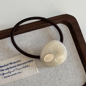 Close-up of brown high-elastic hair tie with gold oval metal and cream geometric detail