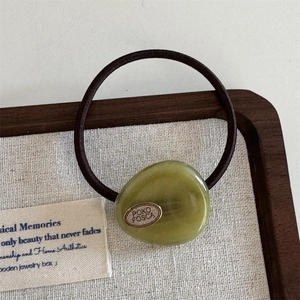 Detail showing an olive green faux gemstone hair tie with an oval metal logo plate