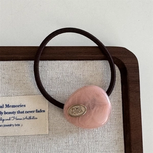 Detail of high-elasticity black hair tie with pink resin bead and golden metal logo tag