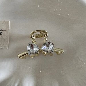 Detail of a golden bow hair claw clip featuring two sparkling heart-shaped rhinestones
