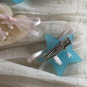 Detail of star-shaped hair clip with light blue resin and pink ribbon bow on metal grip