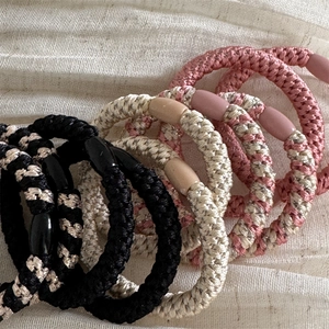 Braided high-elastic hair ties set with resin accents on a textured beige fabric background