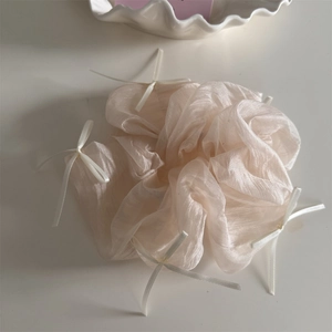 Detail of a ruffled organza scrunchie in apricot with delicate white ribbon bows