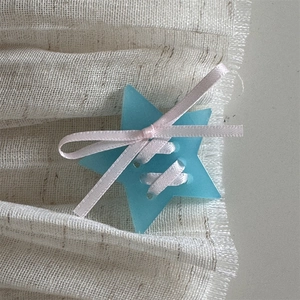 Close-up of blue star hair clip with pink ribbon bow on textured beige fabric