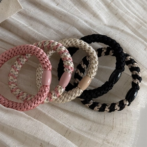 Close-up of four durable woven elastic hair ties in assorted colors on soft cream fabric