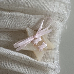 Macro detail of cream star hair clip with pink silk ribbon bow on textured soft fabric