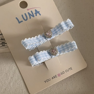 Close-up of blue plaid hair clips with pink heart rhinestone and wavy white lace trim