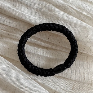 Detailed view of thick braided black elastic hair tie with oval resin bead ornament
