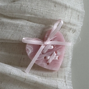 Close-up of pink marble heart hair clip with silk ribbon bow on soft beige fabric