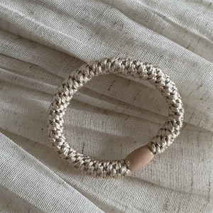 Detail of champagne braided hair tie with a smooth cylindrical clasp on fabric