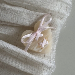 Close-up of heart-shaped hair clip with cream marble texture and pink ribbon detail