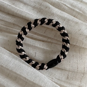 Close-up of woven hair tie with black and champagne gold fibers and smooth oval connector