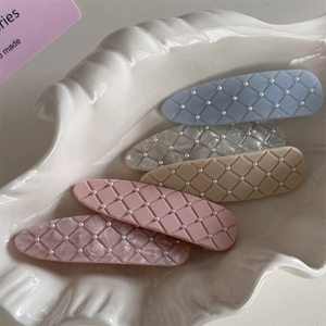 Plaid pattern hair clips with pearls on a decorative shell tray in soft lighting
