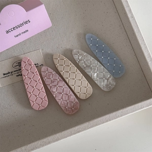 Detail view of five checkered hair clips with mini pearls on a beige textured tray