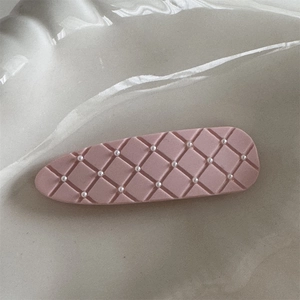 Macro detail of dusty pink lattice hair clip with mini pearls on a shell tray