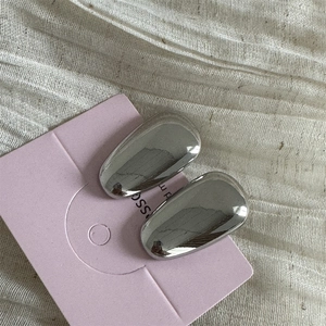 Boucles d'oreilles ovales argentées polies sur carte lilas avec fond en tissu