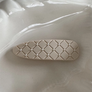 Detailed close-up of a matte beige snap clip featuring quilted pattern and pearl accents