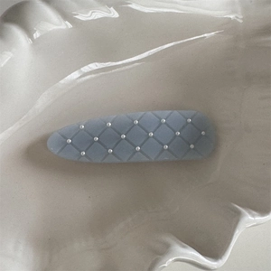 Detail of light blue quilted hair clip with white pearl beads on a ceramic tray