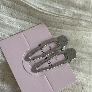 Détail de deux pinces à cheveux argentées style Y2K en métal sur carte rose