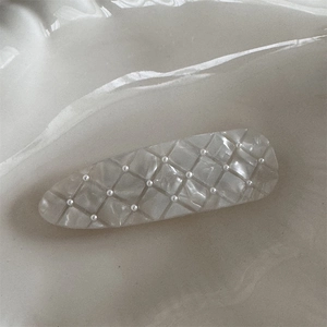 Detail view of cream hair clip featuring textured matte lattice and small pearls