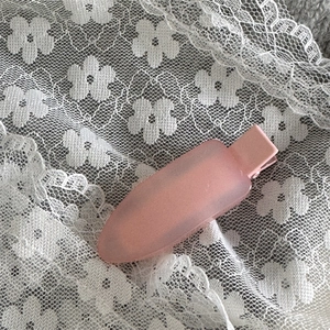 Vue détaillée d'une pince à cheveux rose mat translucide sur un fond de tissu en dentelle