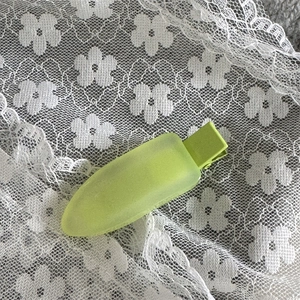 Détail de la barrette à cheveux mate vert lime sur un fond de dentelle florale blanche