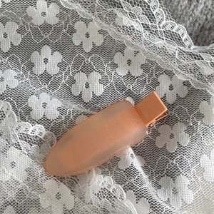 Détail d'une pince à cheveux mate de couleur pêche avec un design en forme de feuille
