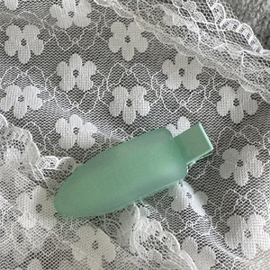 Gros plan d'une pince à cheveux mate vert menthe sur fond de dentelle blanche