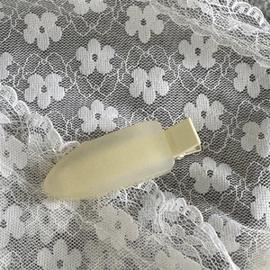 Détail d'une pince à cheveux mate jaune pâle sur dentelle blanche avec texture satinée