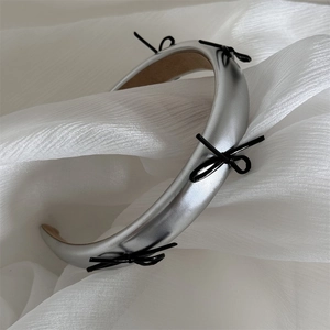 Detail of silver faux leather headband with a glossy black bow on soft white tulle