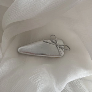 Detailed view of silver metallic bow hair clip on elegant white chiffon fabric background