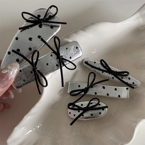 Detail of silver polka dot leather hair clips with black bows on a shell-shaped tray